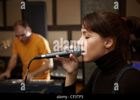 Sänger-Mädchen singt im Studio. Keyboarder in unscharf Stockfoto