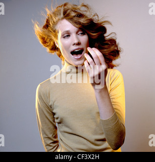 Farben Frauen lange gewellte brünette Haare von Windmaschine, trägt Beige Rollkragen Top, auf die Seite Mund geblasen Stockfoto