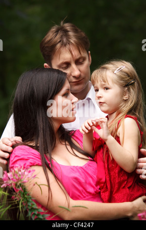 Junge Familie im Sommergarten. Mutter hält Tochter auf Händen. Mann umarmt. Stockfoto