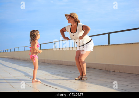 ältere Frau und kleine Mädchen tun Frühsport auf Veranda in der Nähe der Küste Stockfoto