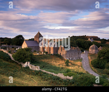 Fading Sonnenlicht beleuchtet die Überreste auf Penmon Priory und Priorat Kirche, die heute als Pfarrkirche dient. Stockfoto