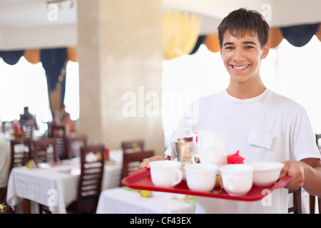 lächelnde leutselig Kellnerjunge hält Tablett mit Gerichte im Restaurant, Weitwinkel Stockfoto