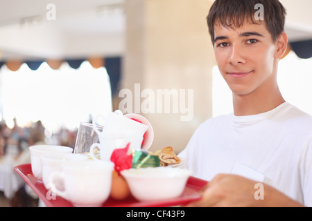 lächelnde leutselig Kellnerjunge hält Tablett mit Gerichten im restaurant Stockfoto