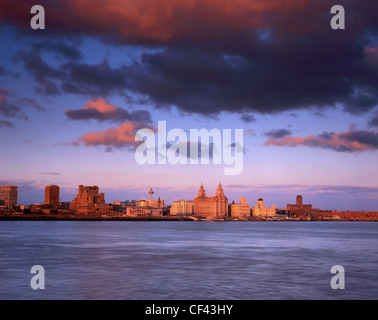 Blick über den Fluss Mersey in Richtung der drei Grazien am Liverpool Wasser bei Sonnenuntergang. Stockfoto