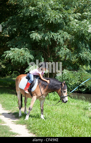 Kleines Mädchen ist ihr Pferd beim Reiten außerhalb in einem Park streicheln. Stockfoto