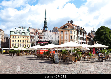 Straßencafés in Domplatz in der Altstadt von Riga mit dem Turm der St.-Petri Kirche im Hintergrund. Stockfoto