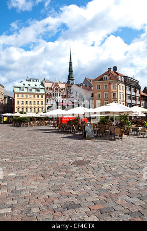 Straßencafés in Domplatz in der Altstadt von Riga mit dem Turm der St.-Petri Kirche im Hintergrund. Stockfoto