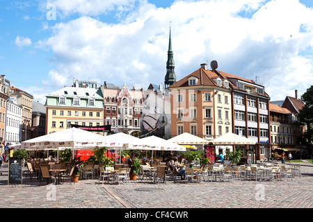 Straßencafés in Domplatz in der Altstadt von Riga mit dem Turm der St.-Petri Kirche im Hintergrund. Stockfoto