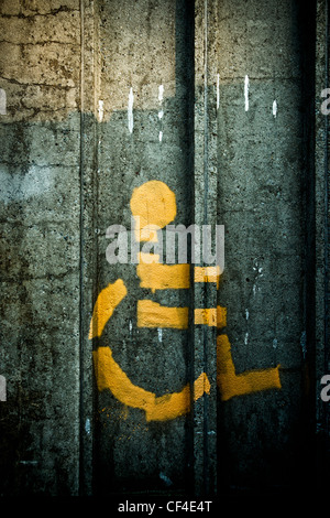 Symbol der Person im Rollstuhl gesprüht auf einer dunklen, alten, baufälligen Steinmauer. Stockfoto