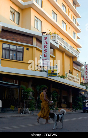 Ein buddhistischer Mönch und ein Hund sind vorbei als Touristenattraktion in Pakse, Provinz Champasak, Laos Pakse Hotel Fuß. Stockfoto