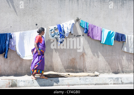 Indische Frau Blick auf Kleidung aufgehängt zum Trocknen auf einem Bürgersteig Wand - Annawadi, Mumbai Stockfoto