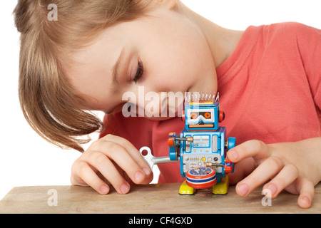 kleines Mädchen im roten T-shirt spielt mit Clockwork Roboter isoliert auf weißem Hintergrund Stockfoto