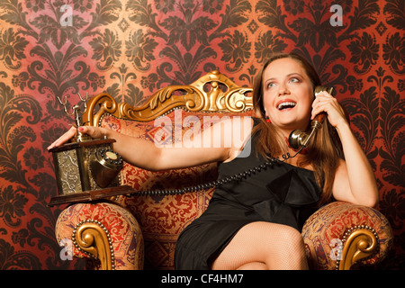 Frau im schwarzen Kleid auf einem Vintage Stuhl sitzen und am alten Telefon. sucht nach hellen Emotionen Stockfoto