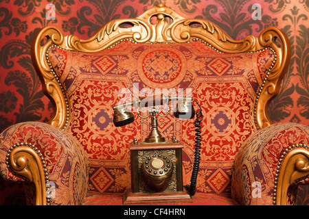 altes Handy ist ein roter Stuhl mit goldenen Akzenten, rote Vintage Tapete. Telefon im Fokus Stockfoto