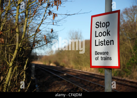 Eine Warnung vor Züge Zeichen an der Seite der Bahnlinie mit einem rasenden Zug nähert sich In Norwich. Stockfoto