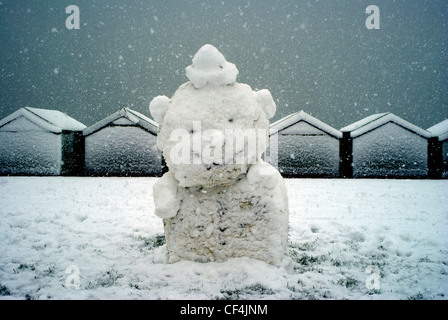 Ein Schneemann auf Hove Rasen mit Schnee bedeckt Strandhütten im Hintergrund. Stockfoto