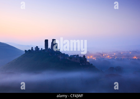 Corfe Castle, aus dem 11. Jahrhundert, erhebt sich über vor Sonnenaufgang Nebel. Stockfoto