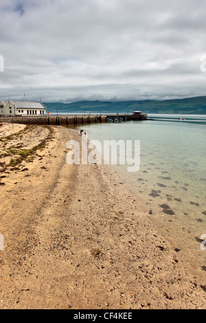 Der Strand neben dem Teil Stein, Teil eisernen Pier in der kleinen Ortschaft Beaumaris über die Menaistraße in Anglesey. Stockfoto