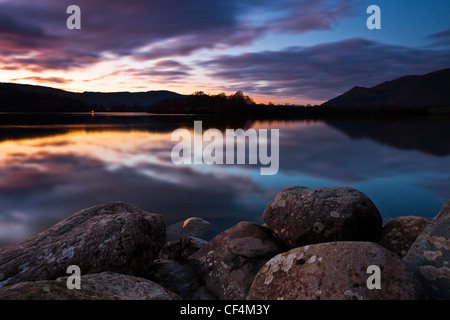 Ein Blick über abgerundete Felsen am Ufer des Derwentwater bei Sonnenuntergang. Stockfoto