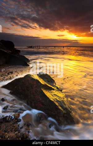 Die Sonne scheint durch einen Bruch in den Wolken bei Sonnenaufgang an der Küste von Norfolk. Stockfoto