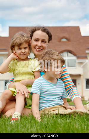 Familie von drei Menschen auf der Wiese vor Haus. Mutter umarmt ihre Tochter und Sohn. Stockfoto