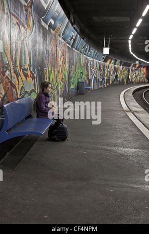 Mädchen mit Teddybär und Box auf einer Bank in einer u-Bahnstation mit Graffiti und wartet. Stockfoto