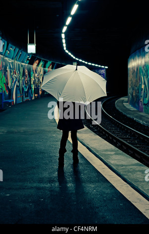 Mädchen mit Regenschirm steht auf einer Plattform zu einer u-Bahnstation mit Graffiti und wartet. Stockfoto