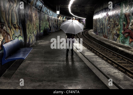 Mädchen mit Regenschirm steht auf einer Plattform zu einer u-Bahnstation mit Graffiti und wartet. Stockfoto