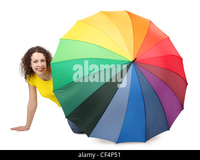 junge attraktive Frau im gelben Hemd sitzt auf weißem Hintergrund und Blick aus bunten Regenschirm isoliert Stockfoto