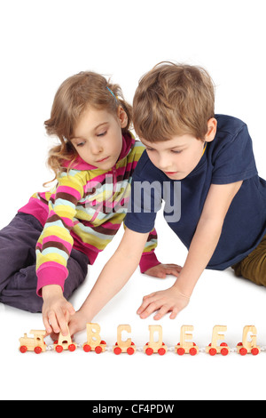 kleine Jungen und Mädchen spielen mit Holzeisenbahn am Boden isoliert auf weiss Stockfoto