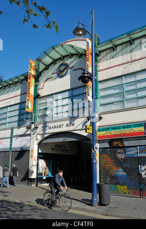 Ein Radfahrer vorbei am Eingang zur Brixton Market Zeile, einer der zwei Arkaden bilden, die zusammen mit einem Straßenmarkt Brix Stockfoto