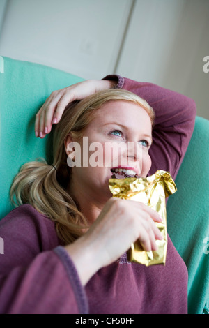 Nahaufnahme eines größeren weibliche blonde Haare aus Gesicht tragen lila Top sitzen im Sessel ein Arm ruht auf Kopf unter Stockfoto