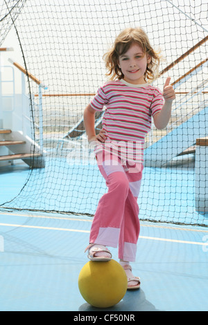 kleines Mädchen mit gelben Ball stehend in der Nähe von Fußballtor auf cruise Liner Deck und diskutiere Geste, Sommertag macht Stockfoto