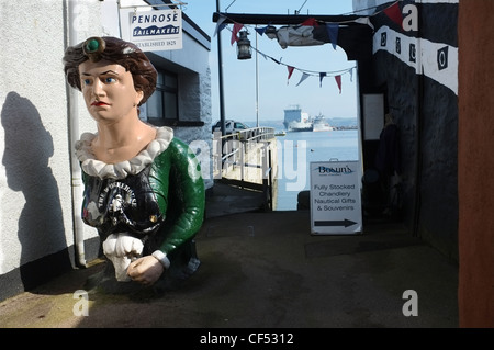 Eine weibliche Galionsfigur in Falmouth neben der Bosuns Locker ein Boot Schiffsausrüster. Falmouth Docks im Hintergrund Stockfoto
