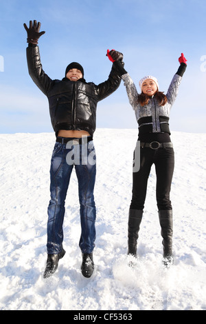 junger Mann und Mädchen springen auf verschneiten Bereich und Lächeln auf den Lippen, Hände halten, Blick in die Kamera Stockfoto