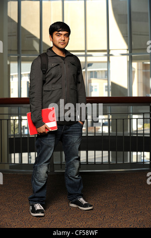 Young ethnischen Student Stand halten ein Heft mit College Gebäude als Hintergrund Stockfoto