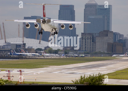 Ein Schweizer Air BAe 146-Flugzeug landet auf dem Flughafen London City Airport mit Docklands und der O2-Arena in der Ferne. Stockfoto