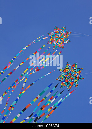 Bunte Drachen reiten auf der Brise vor einem strahlend blauen Himmel Stockfoto