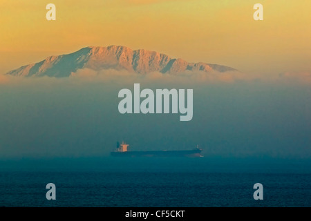 Tarifa, Provinz Cadiz, Spanien. Frachtschiff auf der Durchreise von Gibraltar in der Abenddämmerung. Küste von Marokko im Hintergrund. Stockfoto