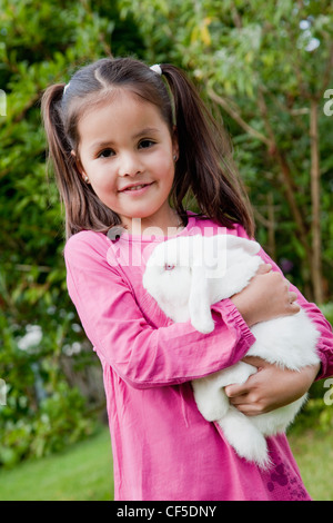 Deutschland, Bayern, Huglfing, Mädchen halten Kaninchen im Garten, Lächeln, Porträt Stockfoto