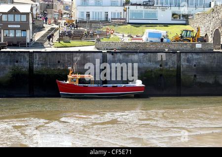 Seehauses Hafen bei Ebbe mit Boot ruhen auf dem schlammigen Meeresboden mit Hafenmeisterei und Leute auf den Bänken sitzen Stockfoto