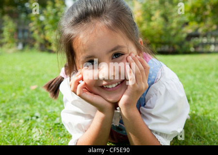 Deutschland, Bayern, Huglfing, Mädchen im Drindl liegen auf dem Rasen im Garten, Lächeln, Porträt Stockfoto