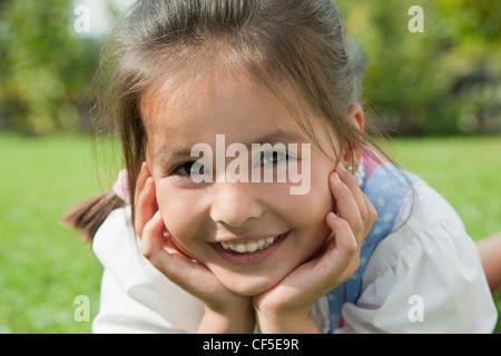 Deutschland, Bayern, Huglfing, Mädchen im Drindl liegen auf dem Rasen im Garten, Lächeln, Porträt Stockfoto