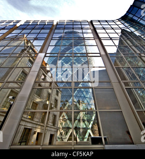 30 St Mary Axe spiegelt sich im Glasbau. Berüchtigt als "Gherkin" wegen seiner 3D ovale Form bekannt, ist es eines der ersten l Stockfoto