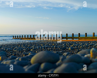 Niedrige Sicht über Kieselsteine in Richtung einer Buhne am Strand von Borth durch die irische See. Stockfoto