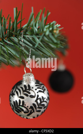 Ein metallisches Silber und schwarz gemustert hängenden Ast einen Weihnachtsbaum, eine schwarze Kugel dahinter, eine rote Kugel Stockfoto