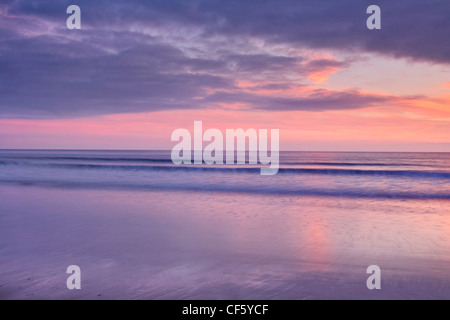 Wellen auf den Strand unten lila Himmel bei Sonnenuntergang überrollen Marloes Sands. Stockfoto