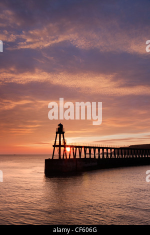 Sonnenaufgang über dem Meer hinter dem Pier Ost und Leuchtturm Whitby an der Küste von Yorkshire. Stockfoto