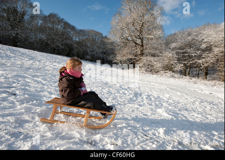 Ein junges Mädchen rutscht Schnee bedeckten Hang auf einer traditionellen Holzschlitten. Stockfoto