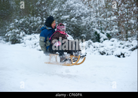 Mutter und Tochter, die Spaß im Schnee auf einem traditionellen Holzschlitten. Stockfoto